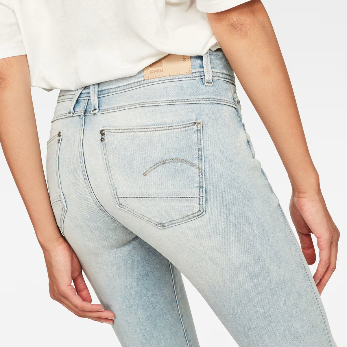 Detail shot of light blue skinny jeans highlighting the back pocket and mid waist on a white background.