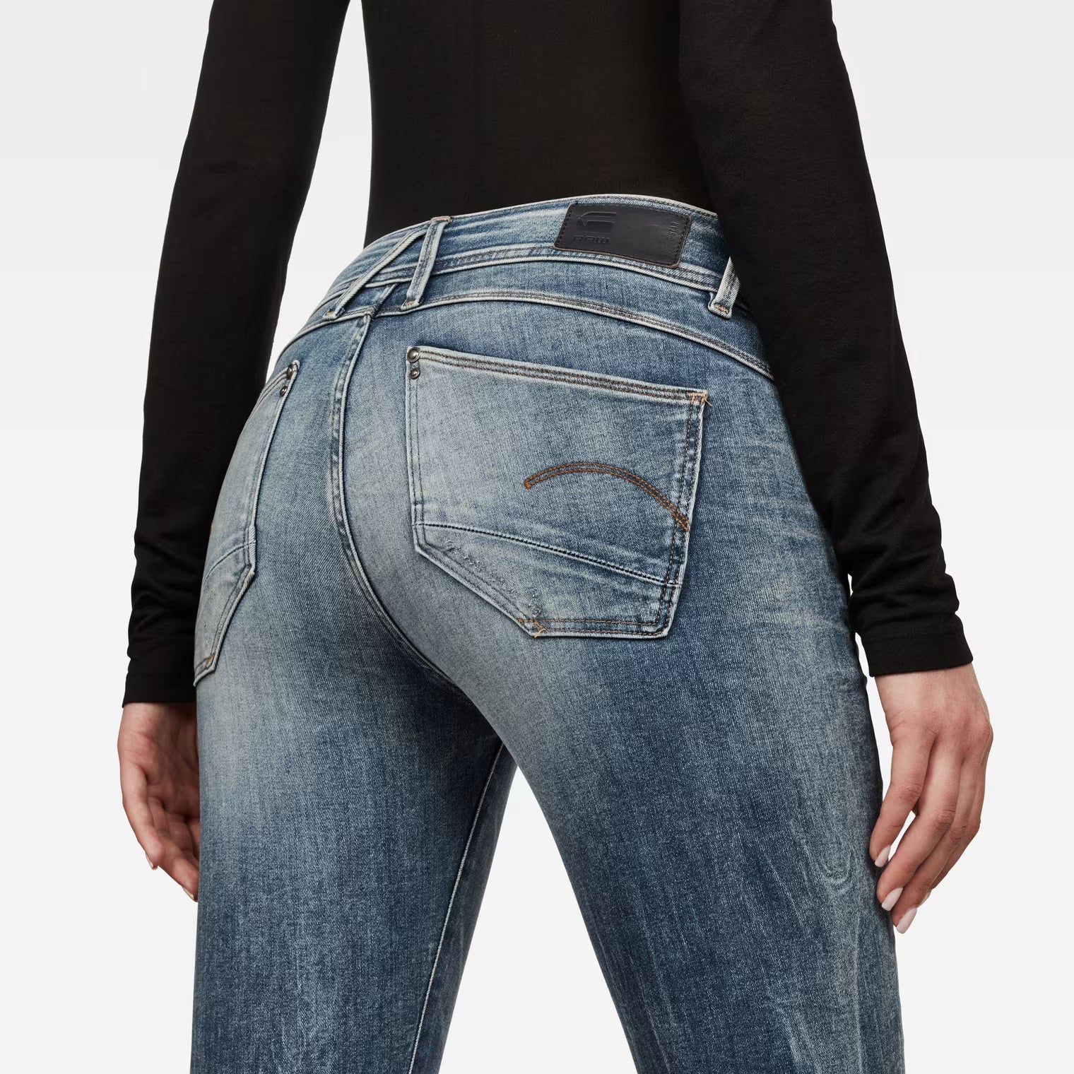 Back view of light blue skinny jeans with a mid waist displayed against a white background