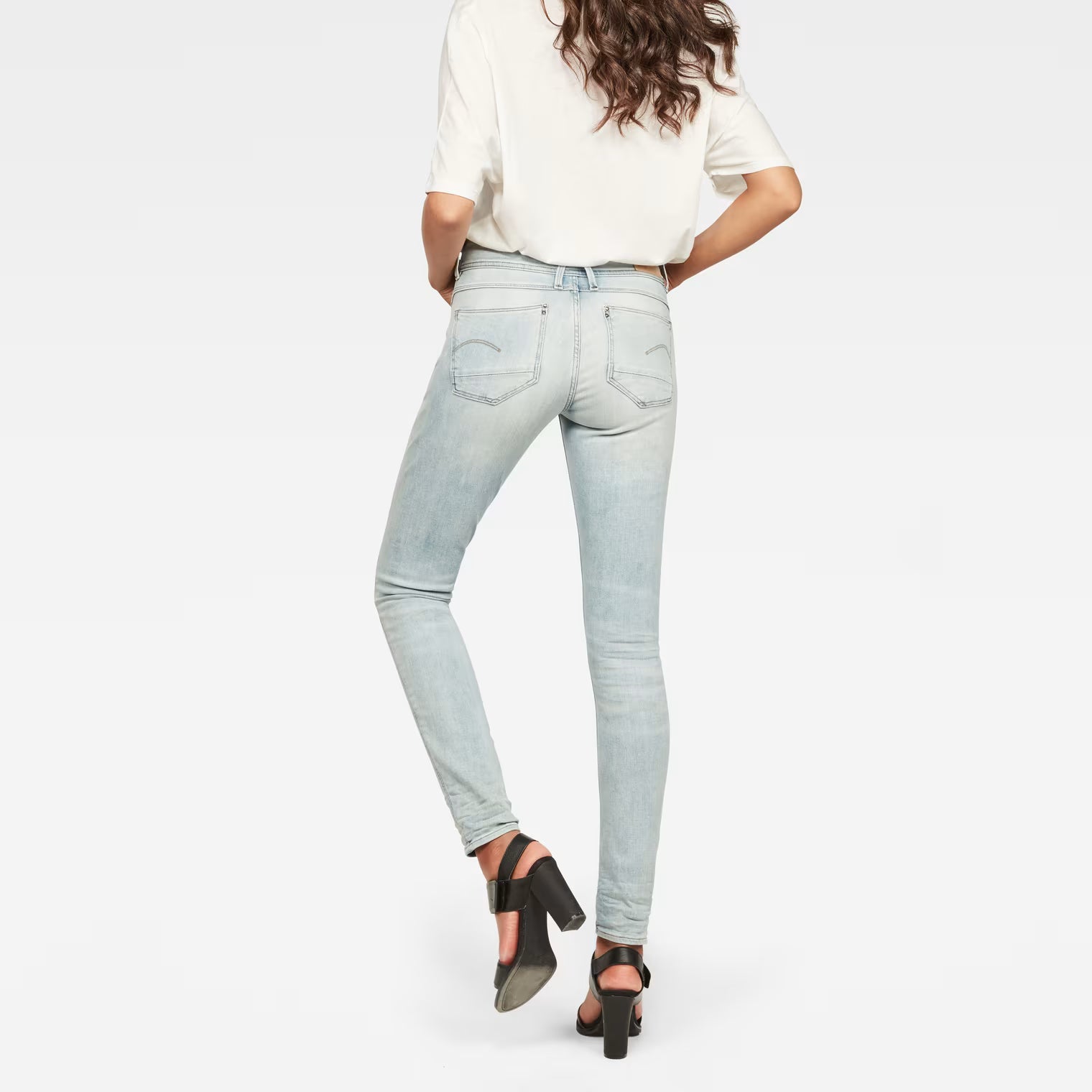 Back view of light blue skinny jeans featuring a mid waist on a white background.