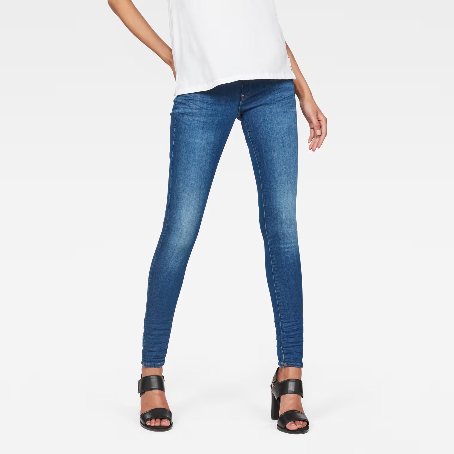 Lifestyle shot of blue skinny jeans with mid waist on a white background
