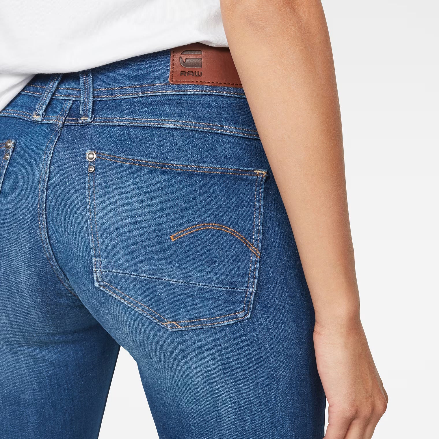 Detail close-up of blue skinny jeans showing back pockets and stitching on a white background