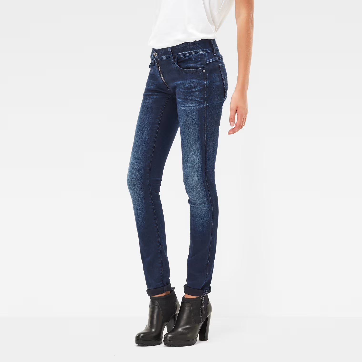 Side view of dark blue skinny jeans featuring a mid waist and zipper detail on a white background.