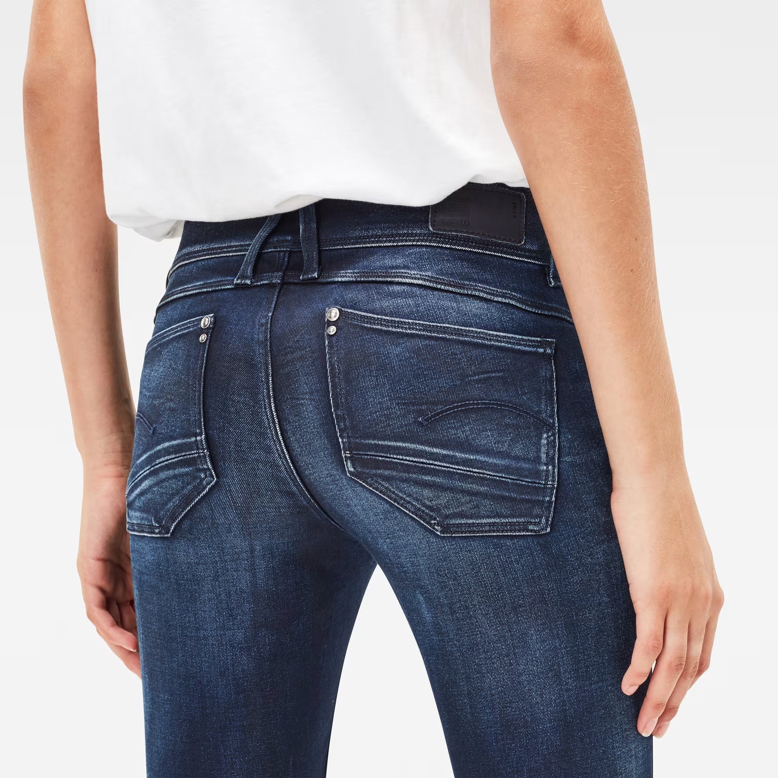 Detail close-up of dark blue skinny jeans highlighting zipper detail and skinny fit on a white background.
