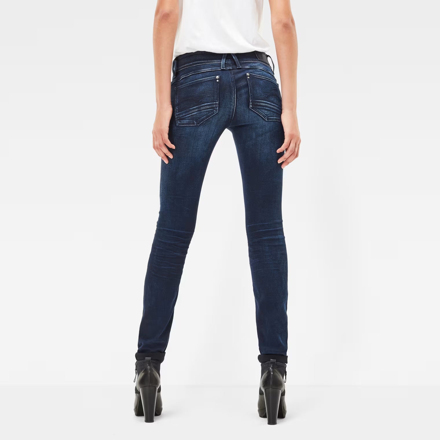 Back view of dark blue skinny jeans showcasing a mid waist and skinny fit on a white background.