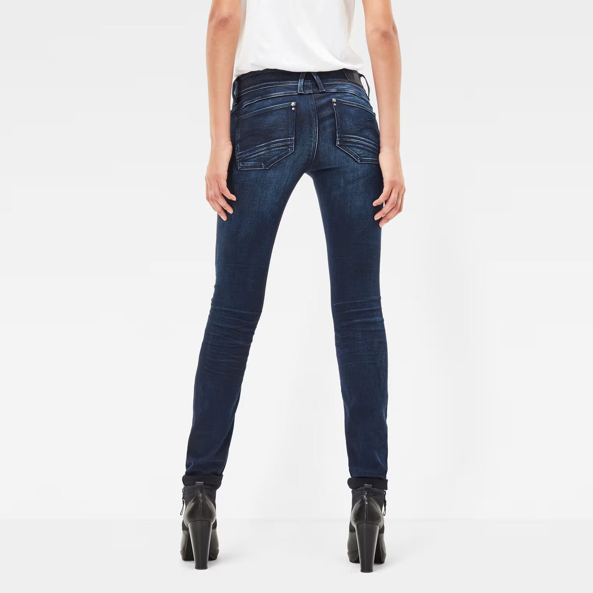 Back view of dark blue skinny jeans showcasing a mid waist and skinny fit on a white background.