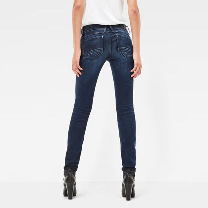 Back view of dark blue skinny jeans showcasing a mid waist and skinny fit on a white background.