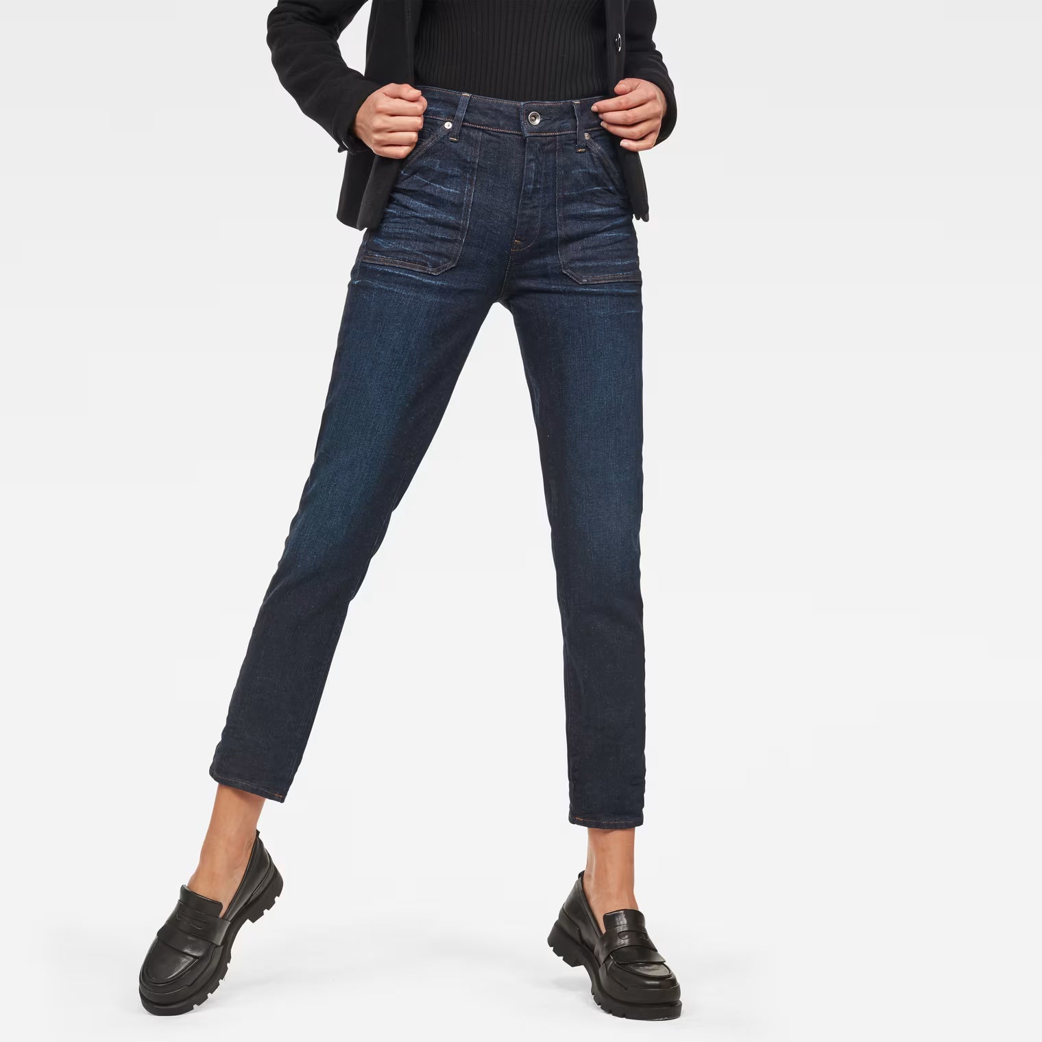 Lifestyle shot of dark blue high waist straight ankle jeans against a white background.