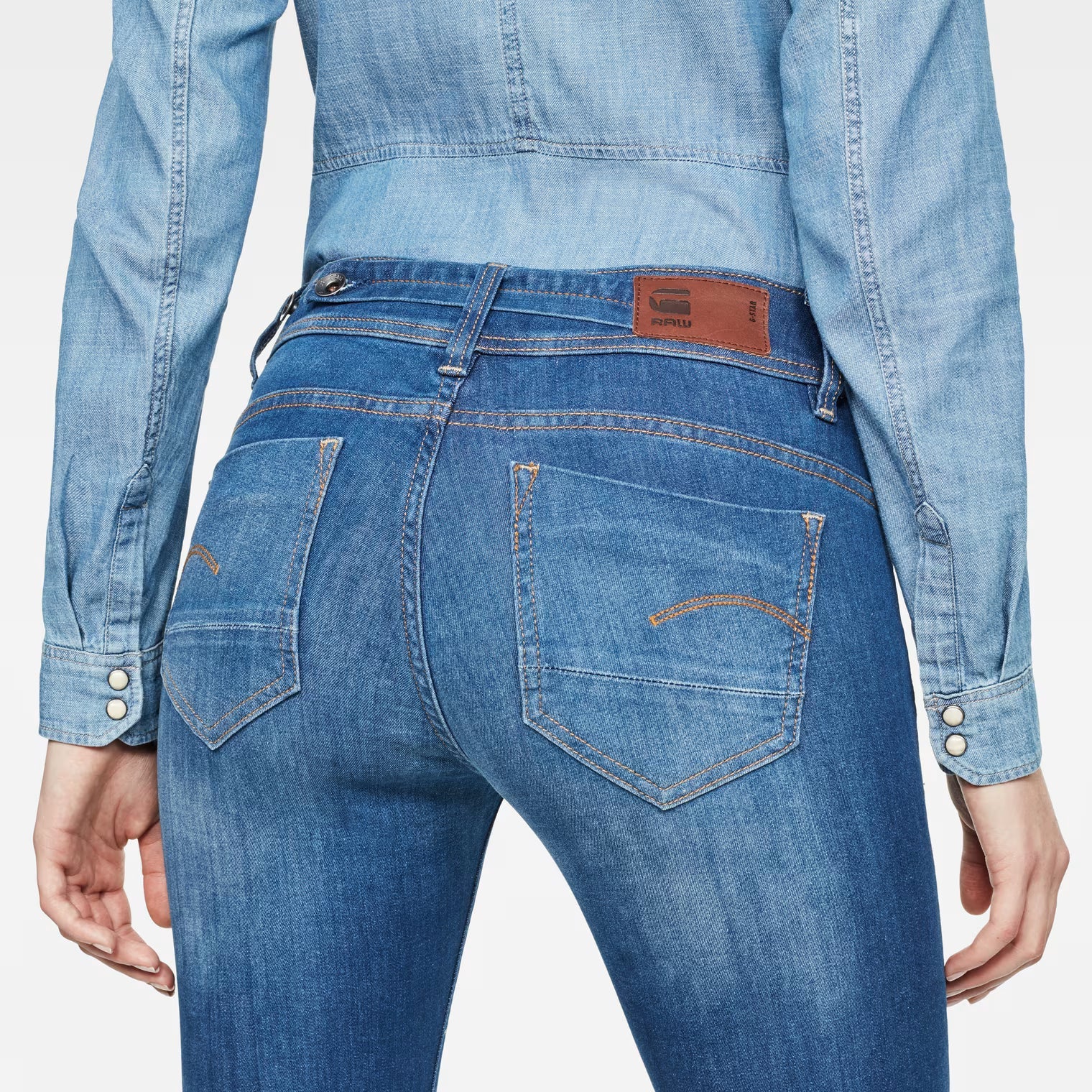 Detail close-up of medium blue jeans highlighting back pockets and a brown label on a white background.