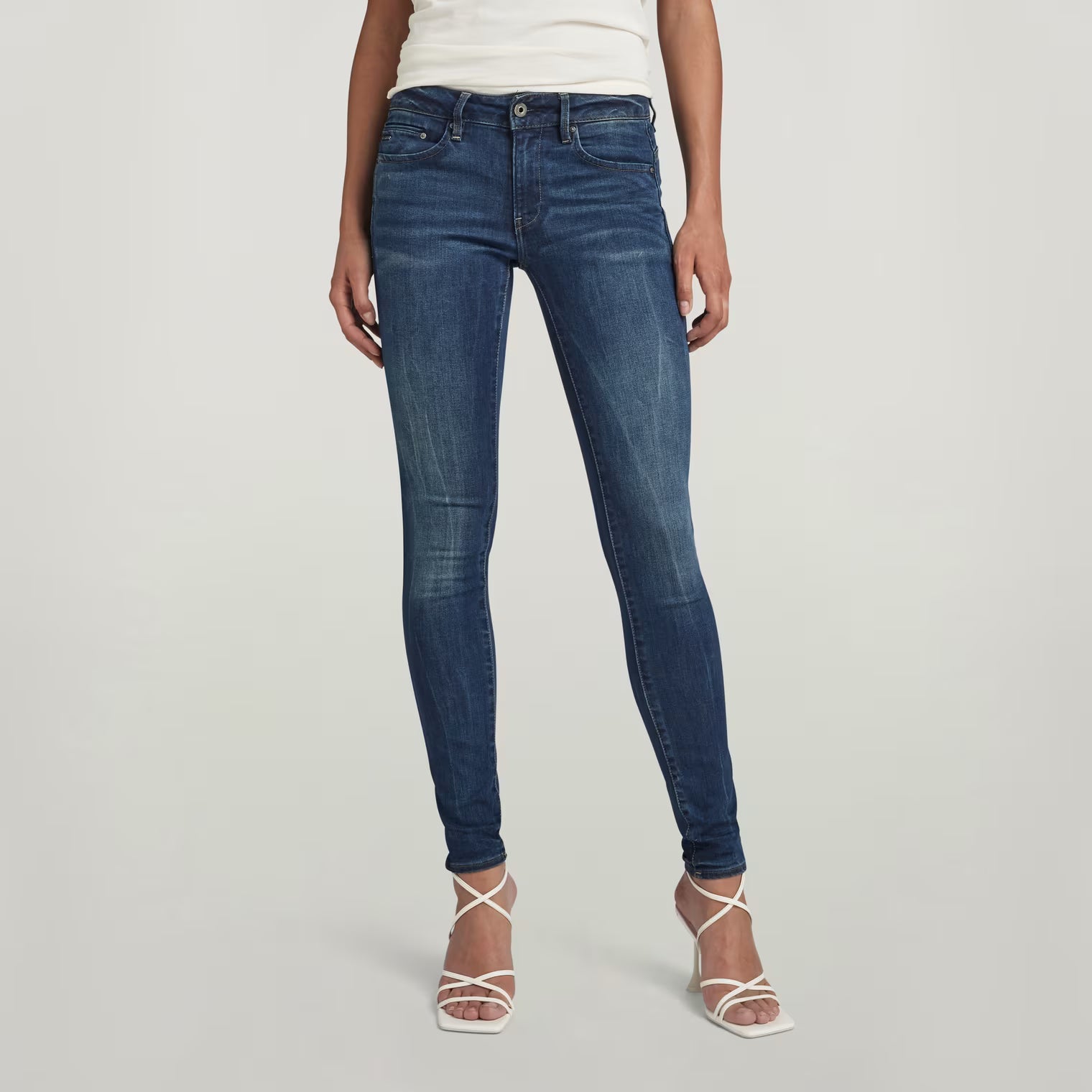 Front view of dark blue skinny jeans featuring a mid waist design on a white background.