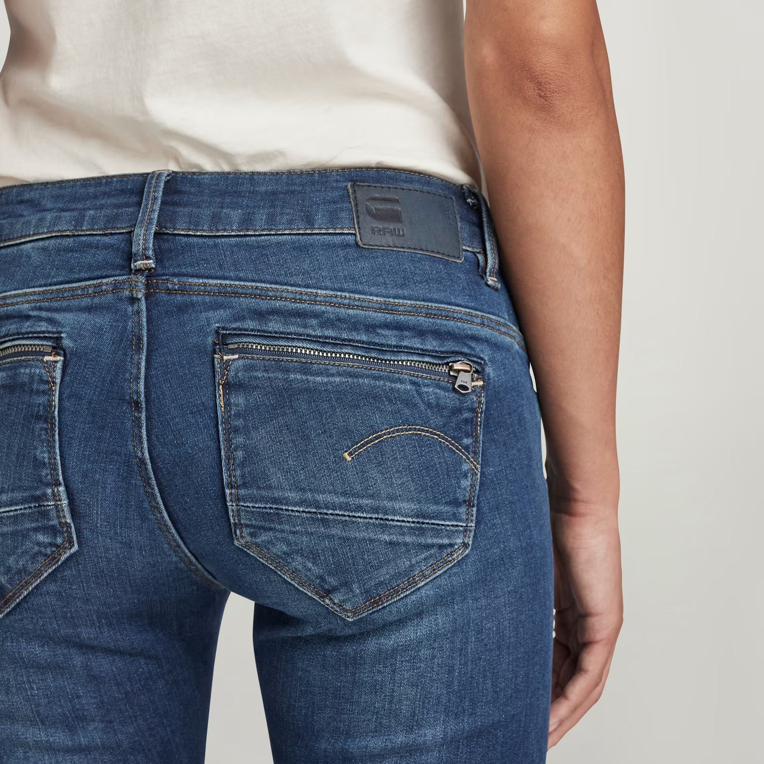 Detail shot of dark blue skinny jeans highlighting back pockets on a white background.
