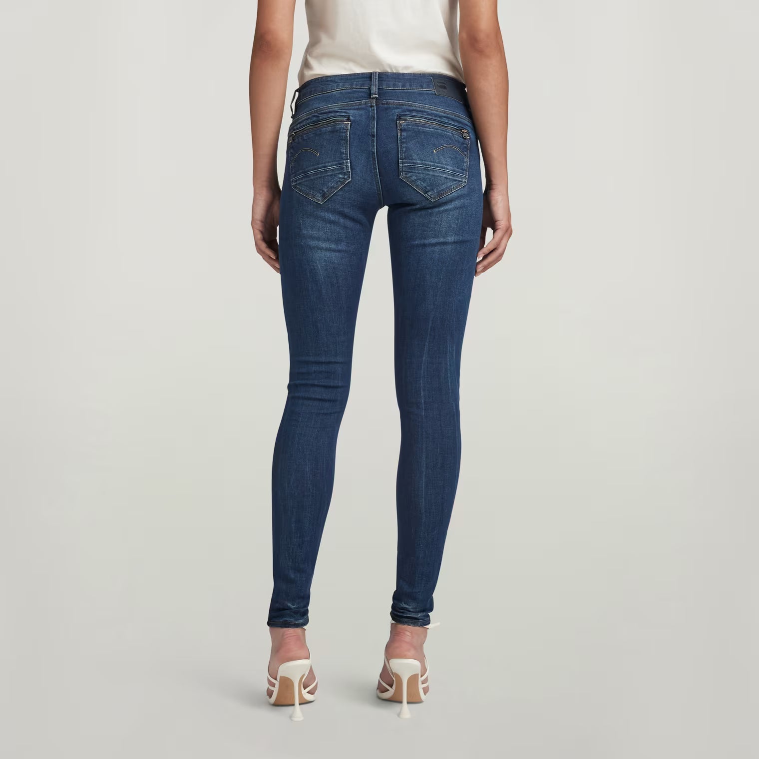 Back view of dark blue skinny jeans showcasing the mid waist fit on a white background.