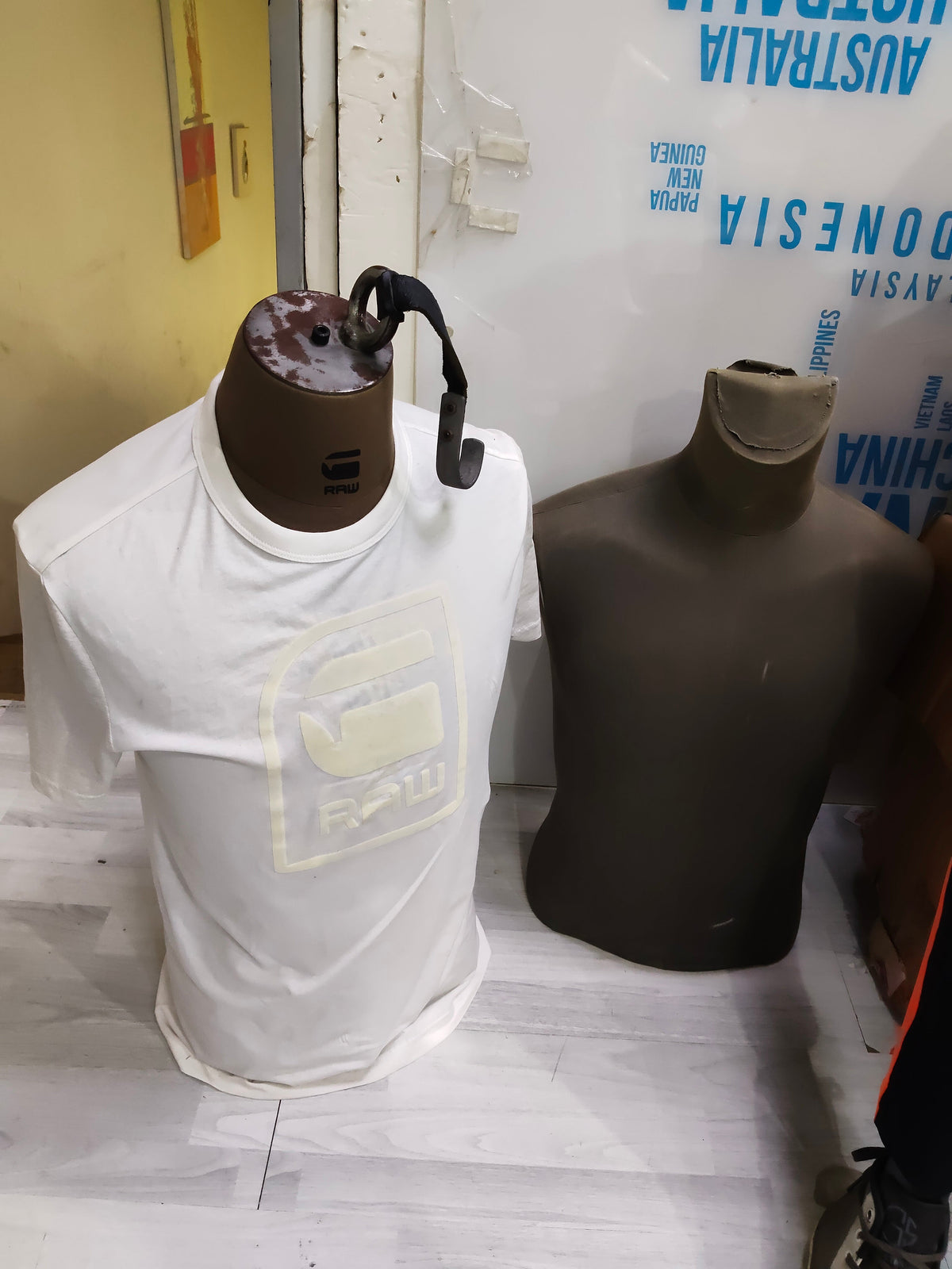 Male torso mannequins in white tee and bare dark form, in storage