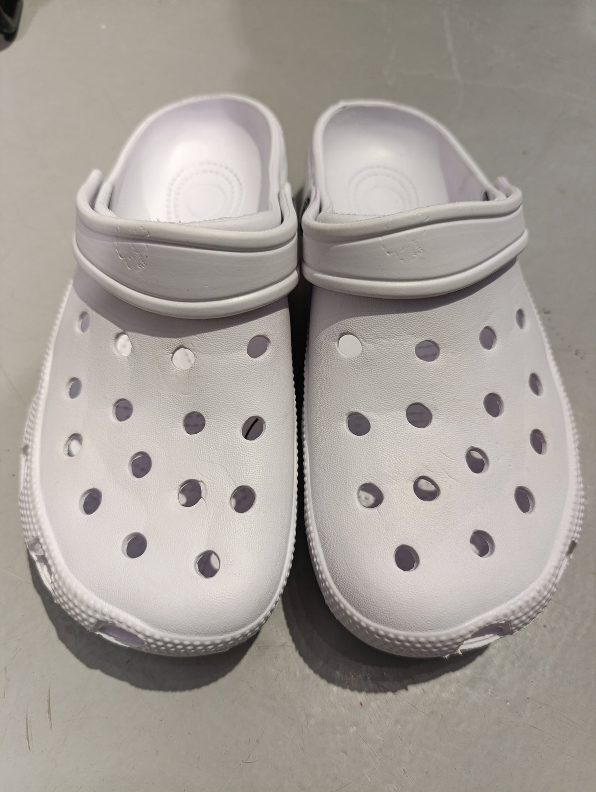 Pair of white foam clogs on a grey floor