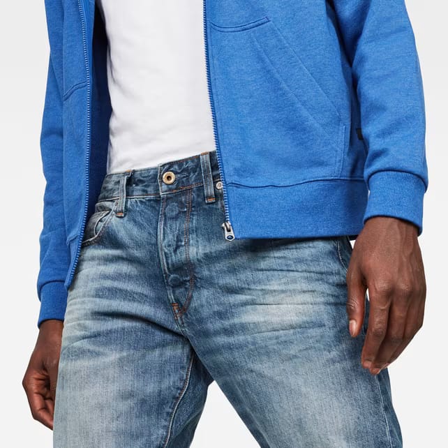 Close-up detail of blue distressed jeans focusing on distressed features on a white background.