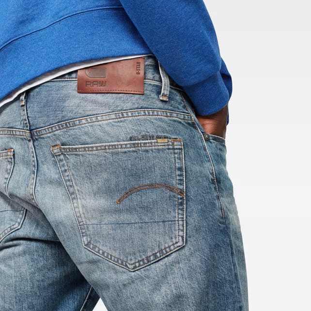 Detail shot of the back pocket of blue jeans with leather patch and stitching on a white background.