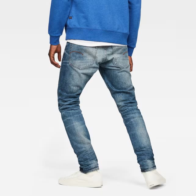 Back view of blue jeans with a faded denim look on a white background.